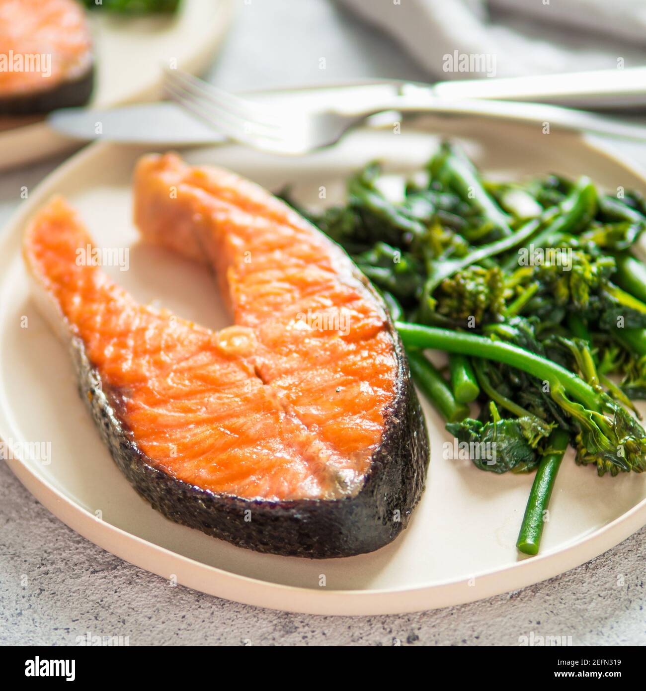 Ready-to-eat grilled salmon steak and greens - baby broccoli or broccolini and spinach on rustic craft plate over gray background. Keto diet dish. Stock Photo