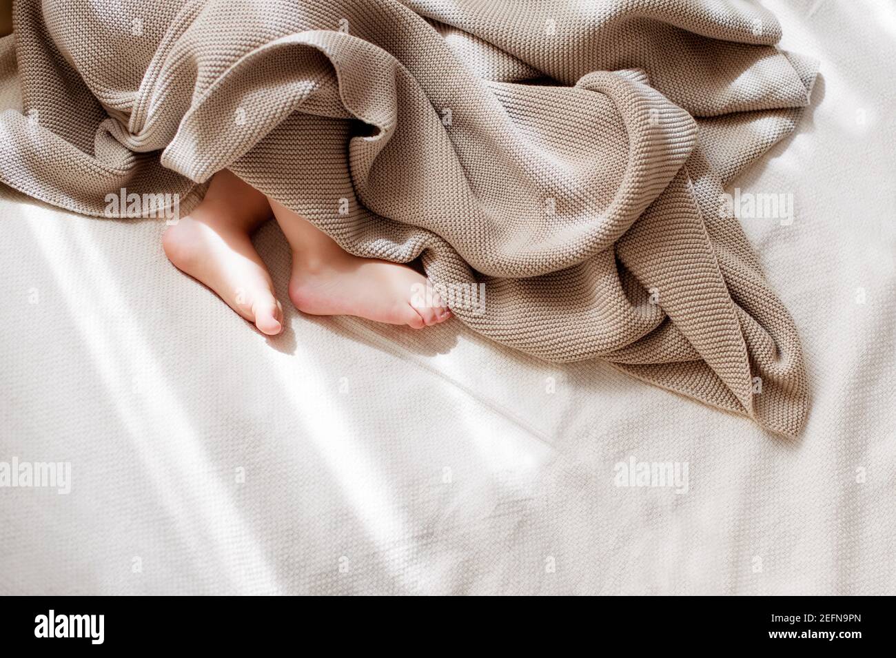 Baby little feet covered with lightweight cotton baby knit blanket Stock Photo