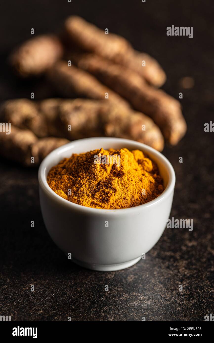 Indian turmeric powder and root. Turmeric spice. Ground turmeric in bowl on black table. Stock Photo