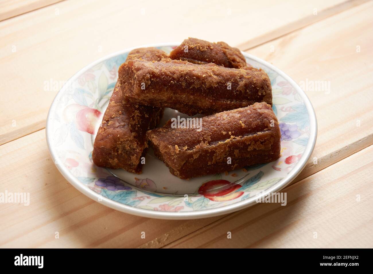 Panela slices in a small plate on wooden table. Also known as rapadura, it is unrefined whole cane sugar typical of Central and Latin America. Stock Photo