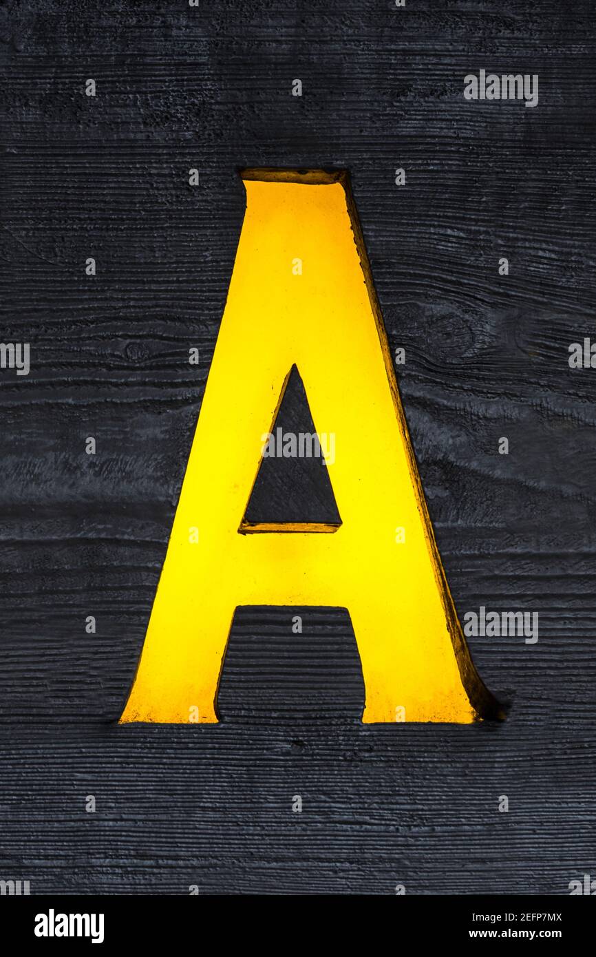 Yellow backlit letter A sawn out of a wooden board Stock Photo