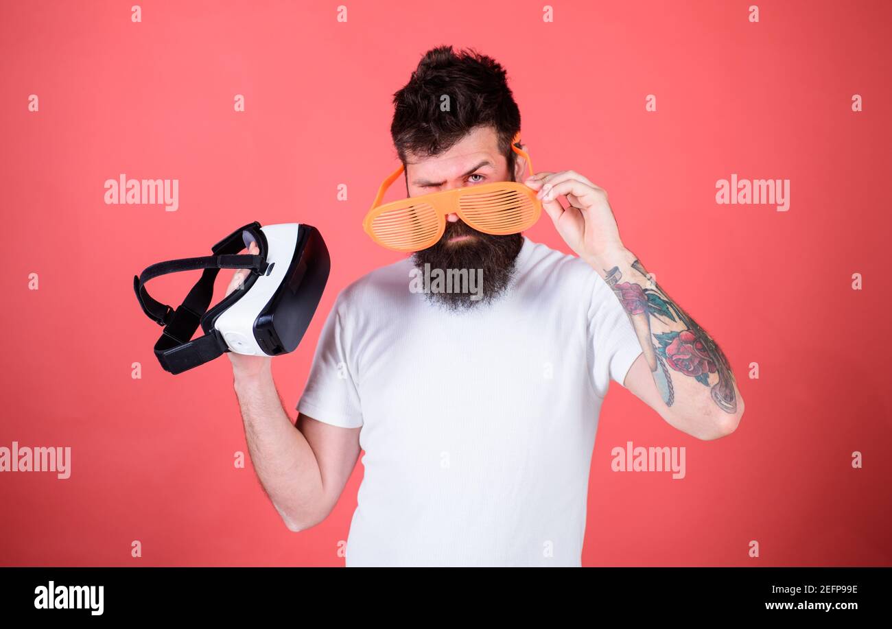 Which glasses choose louvered or virtual. Man bearded hipster with virtual reality headset and louvered sunglasses red background. Alternative reality. Man making decision what choose real or virtual. Stock Photo