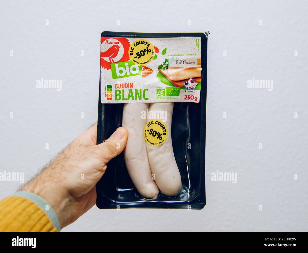 Paris, France - April 9, 2020: POV male hand holding Bio oRganic Boudin blanc sausage against white kitchen background with DLC sticker Stock Photo