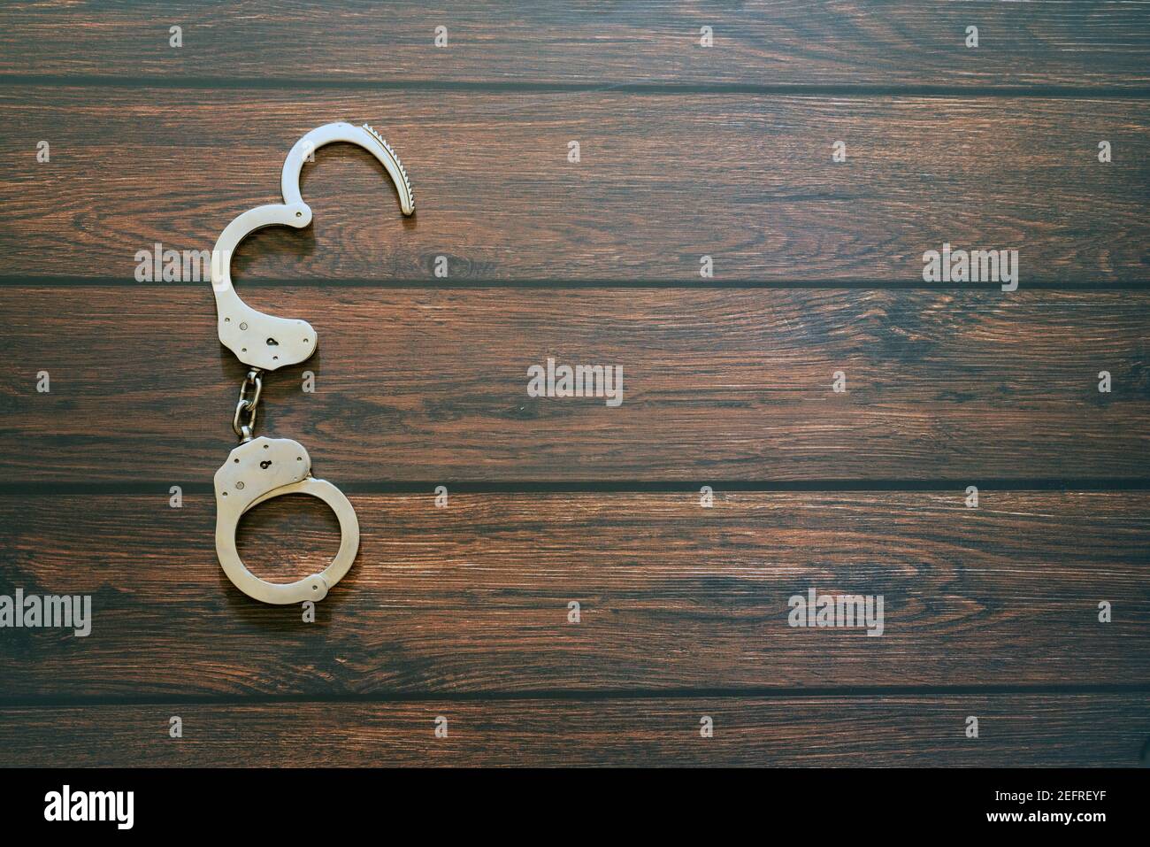 Handcuffs with an open part on a wooden board Stock Photo