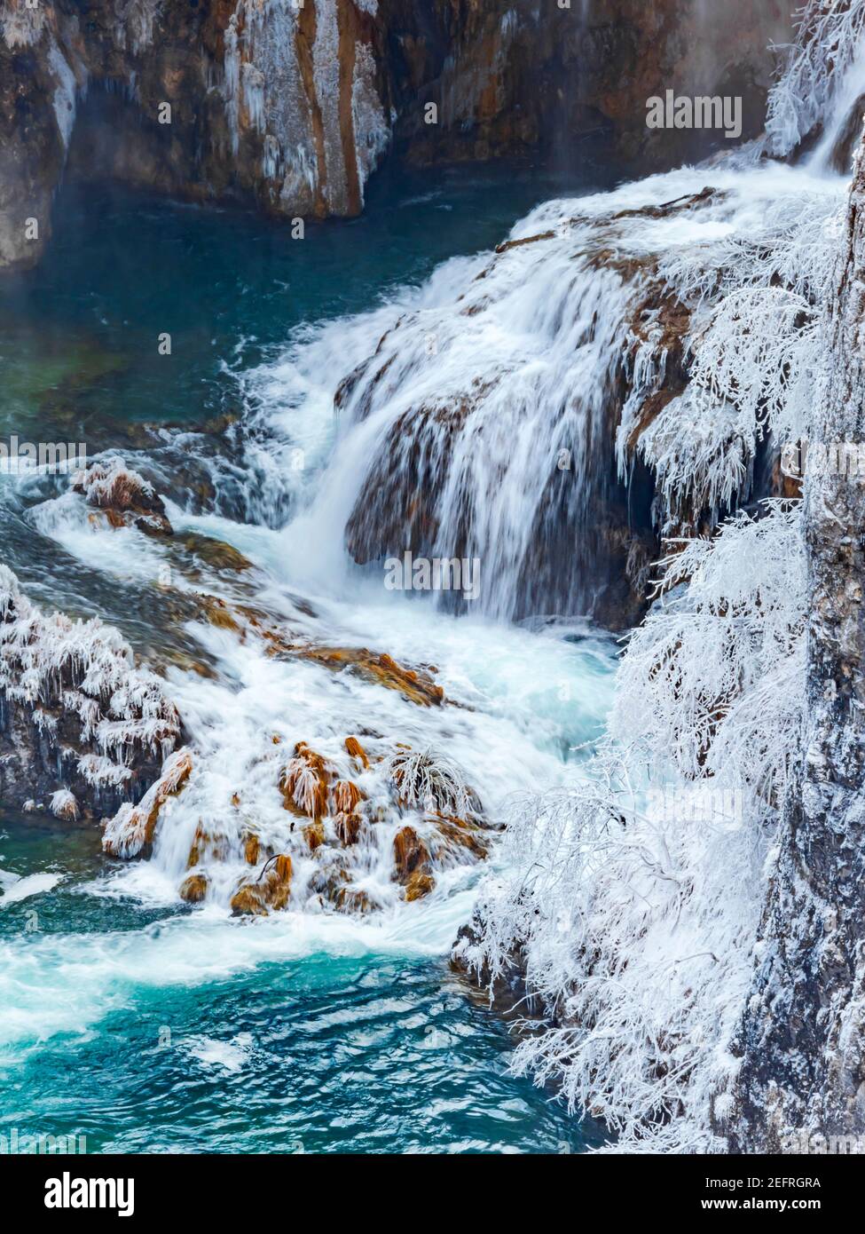 Dynamic Winter season waterfalls in Plitvice lakes Croatia Europe with snow ice waterflow flowing flow atop rocky rough terrain sprinkling water Stock Photo