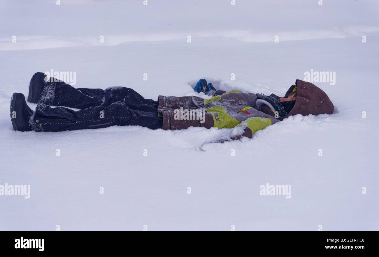A young boy (8 yr old) lying on his back in deep snow Stock Photo