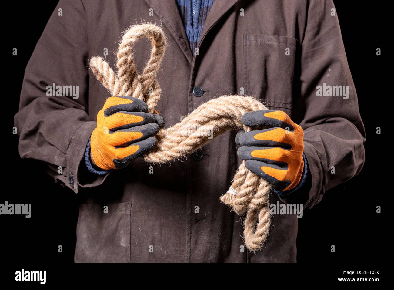 A production worker holding a thick rope in his hands. Construction worker working on the construction site. Dark background. Stock Photo