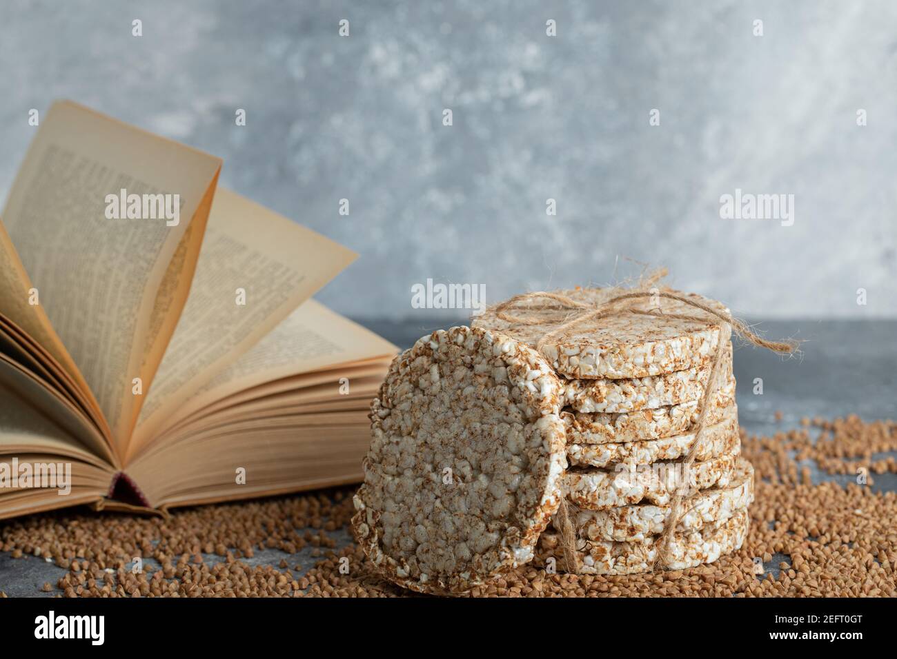 Delicious crispbread, uncooked buckwheat and book on marble surface