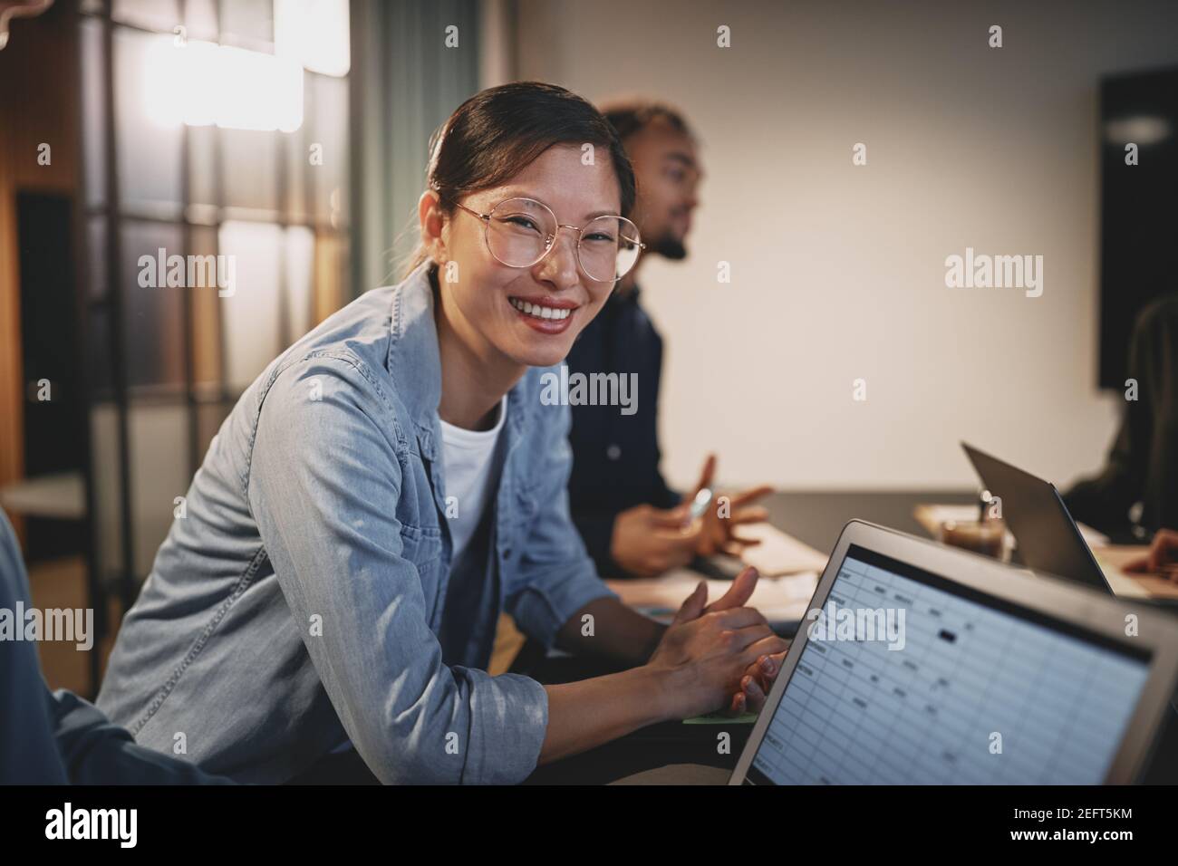 Smiling young Asian businesswoman leaning on a table during a meeting with a colleagues in an office Stock Photo