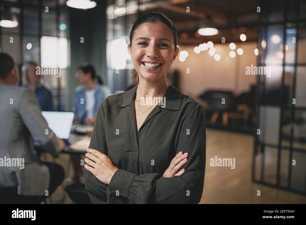 Young businesswoman smiling while sitting in an office with coworkers working together in the background Stock Photo