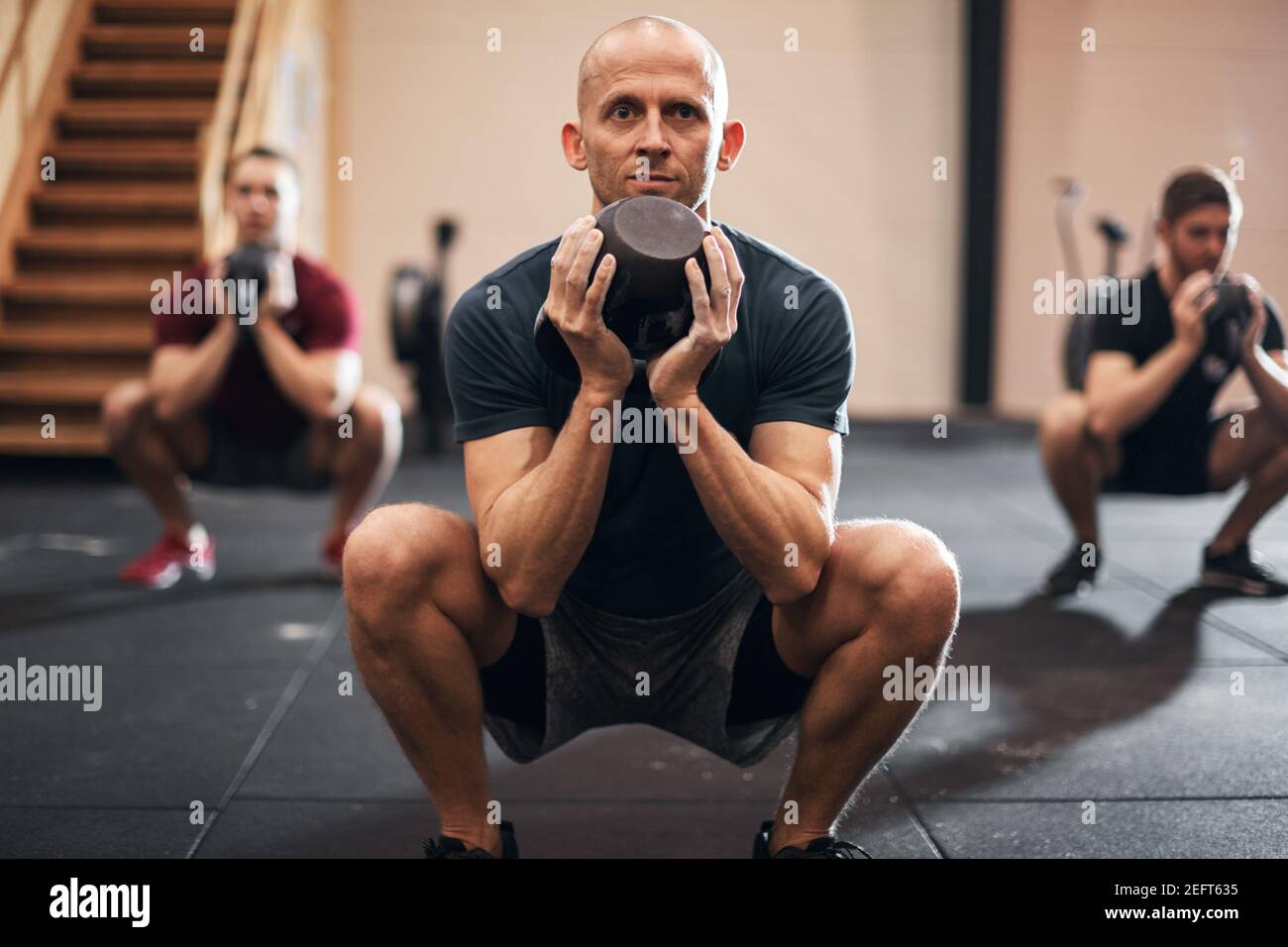 Fit man in sportswear doing squats with weights during a strengthening class at the gym Stock Photo