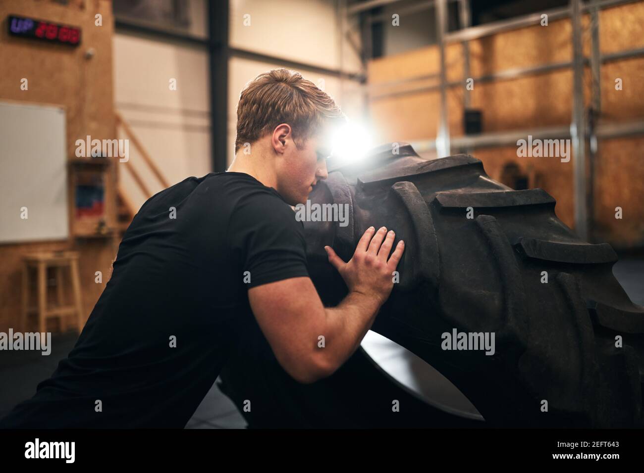 Fit young man in sportswear flipping a heavy tire across a gym during an intense workout at the gym Stock Photo