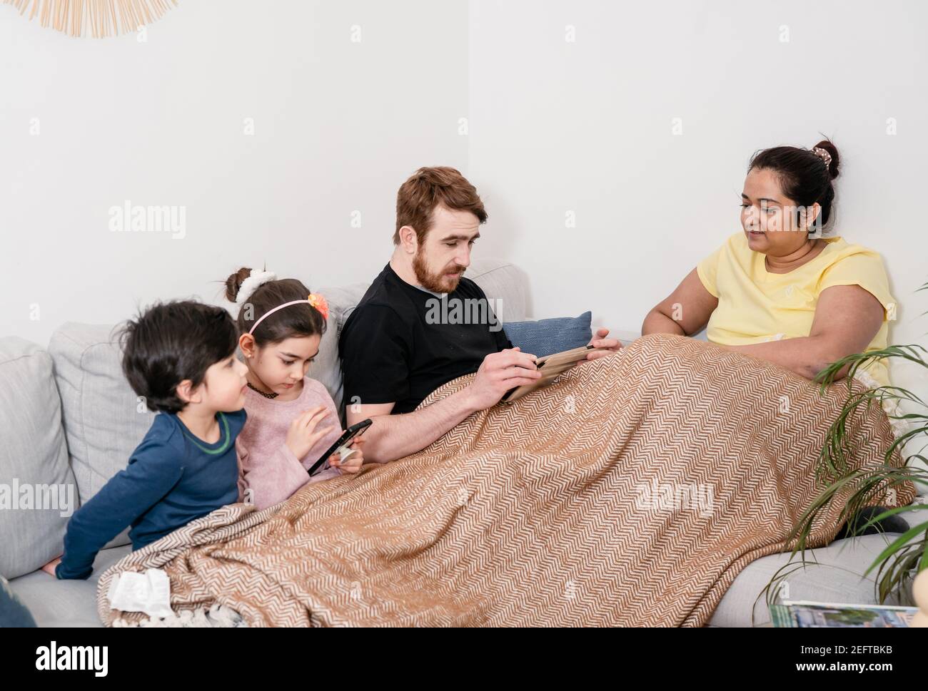 Young multinational family relaxing at home with digital devices Stock Photo