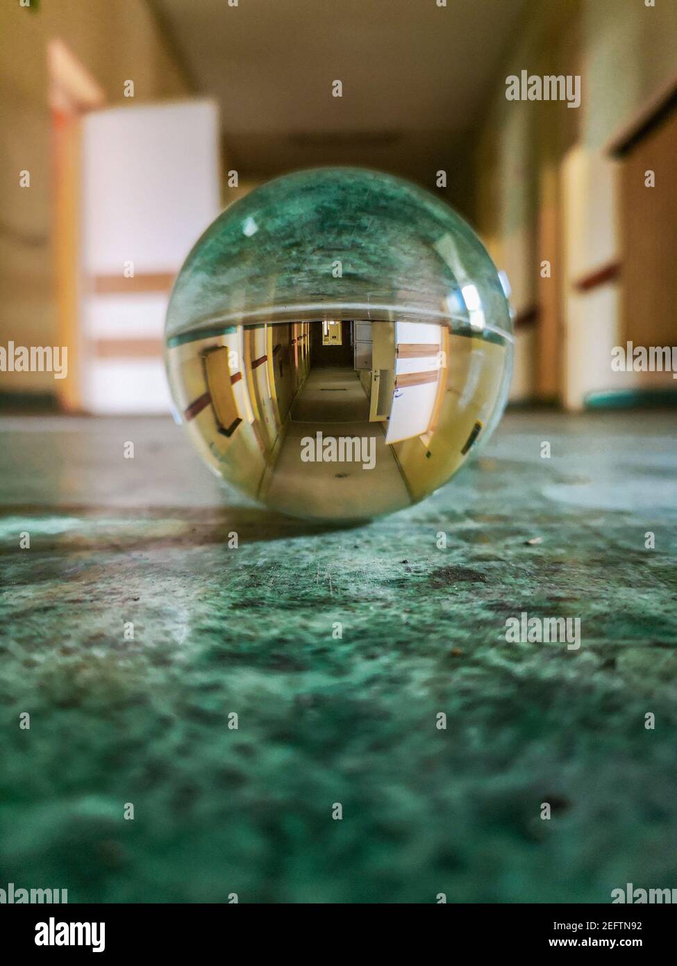 Long corridor with green covering on the floor reflected in crystal glassy lensball in old abandoned hospital Stock Photo