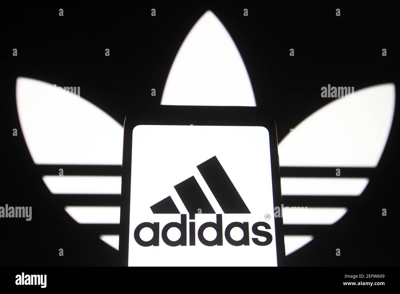 In this photo illustration the Adidas logo is seen on a smartphone and a pc  screen Stock Photo - Alamy