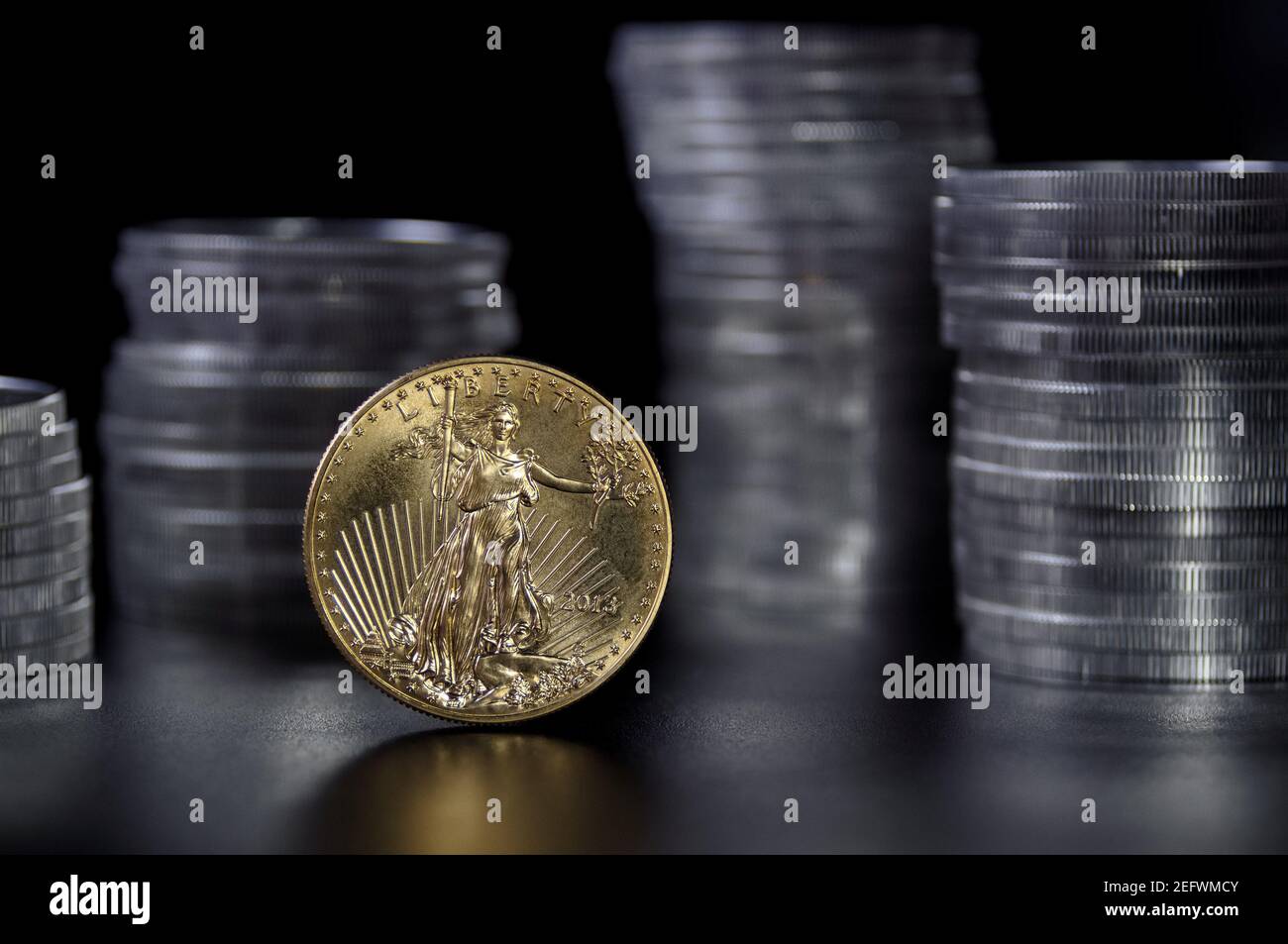 A one ounce gold coin in front stacks of 1 ounce American silver Eagle coins Stock Photo