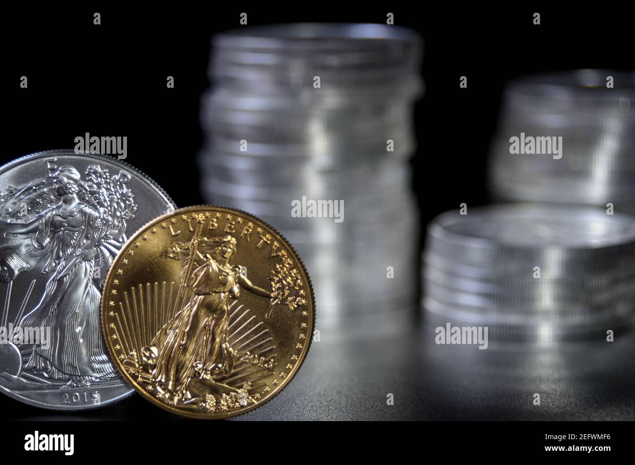 In focus gold and silver american eagle coin with out of focus stacks of silver eagle coins in the background Stock Photo