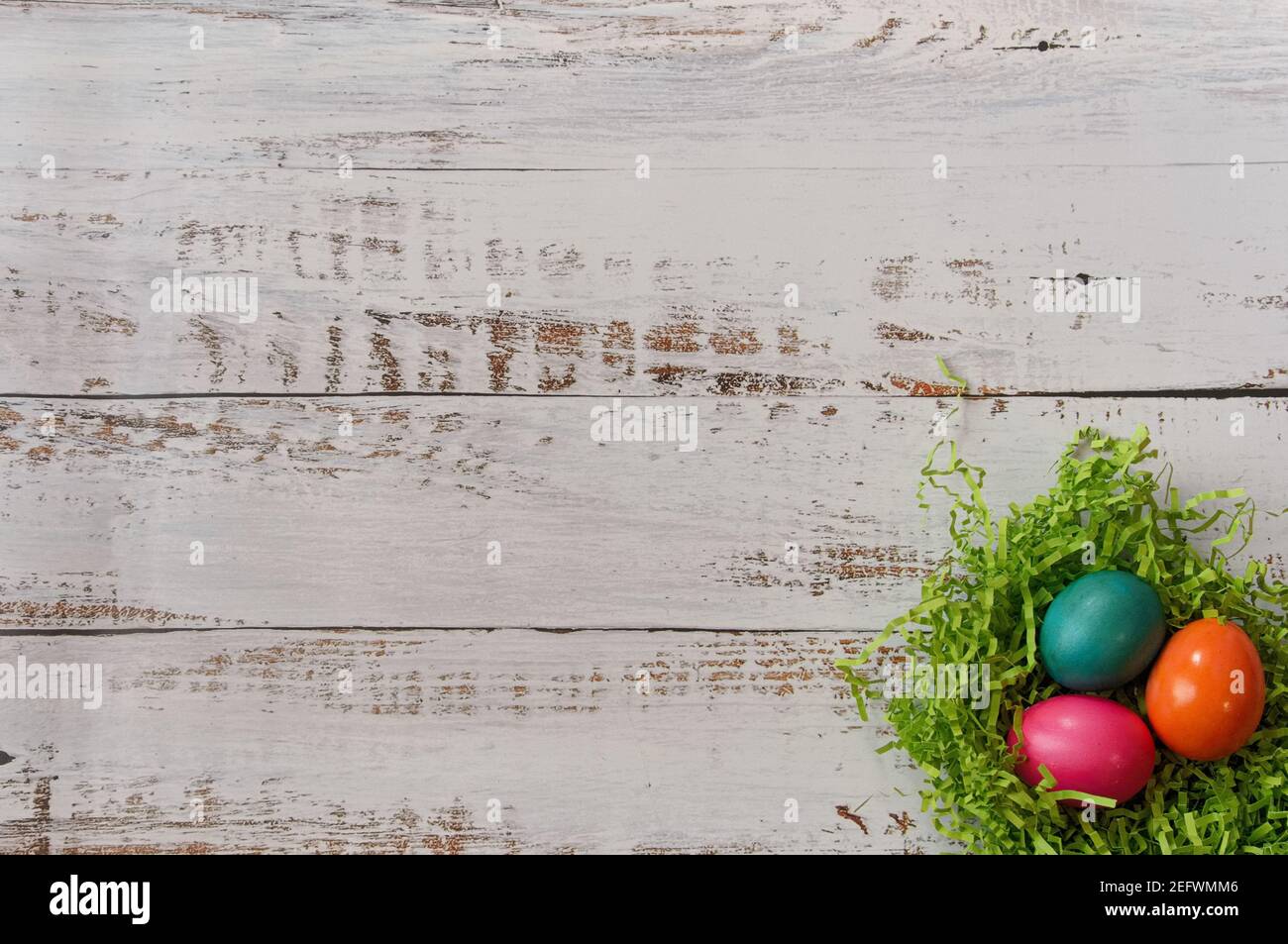 Three colorfully painted easter eggs in an easter grass nest in lower right corner of a white wooden background, with copy space Stock Photo