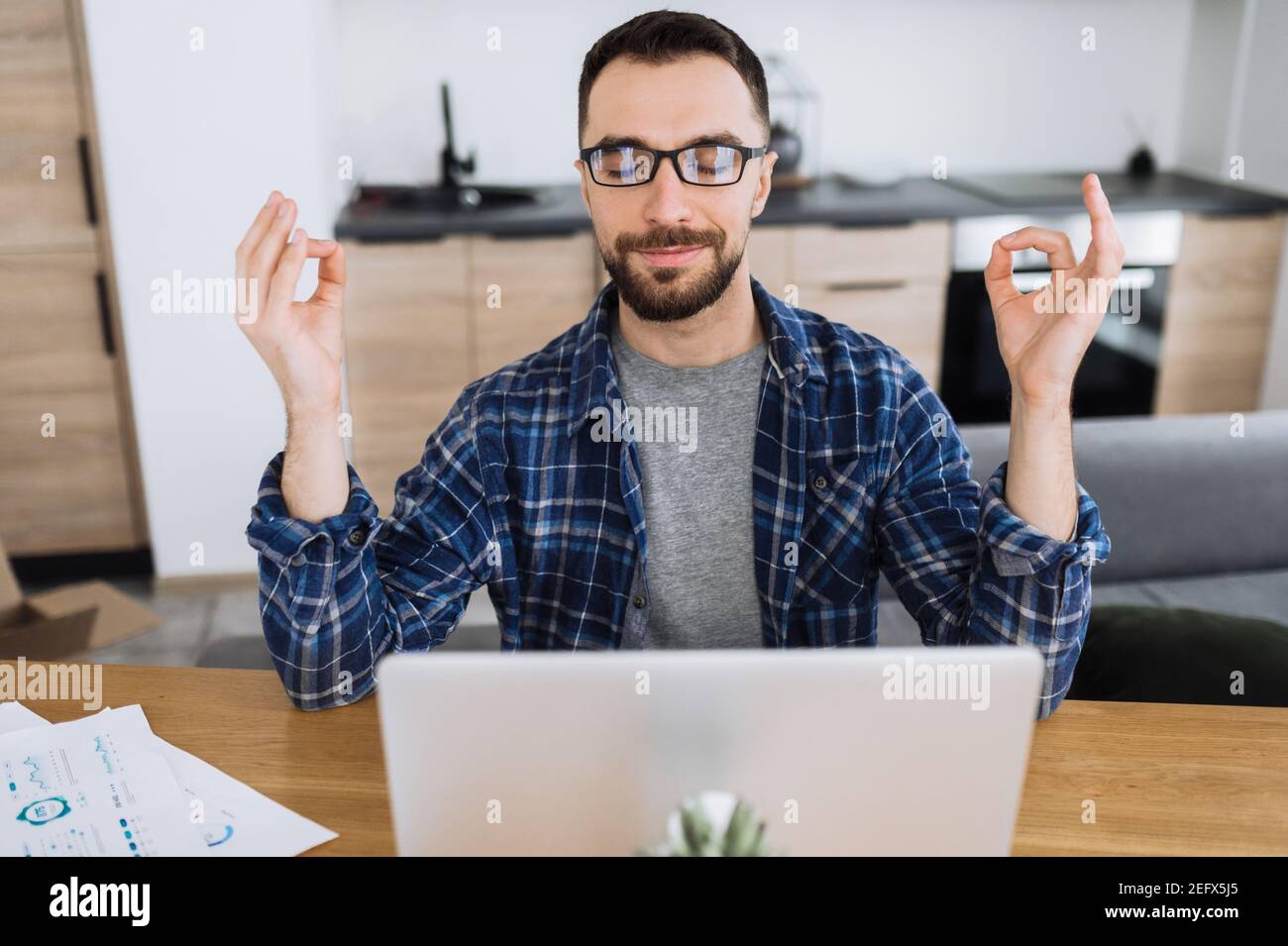 Successful male freelancer working from home office. Confident young entrepreneur sits at the desk, meditate, charging by good energy, calm down, through out negative emotions, taking break from work Stock Photo