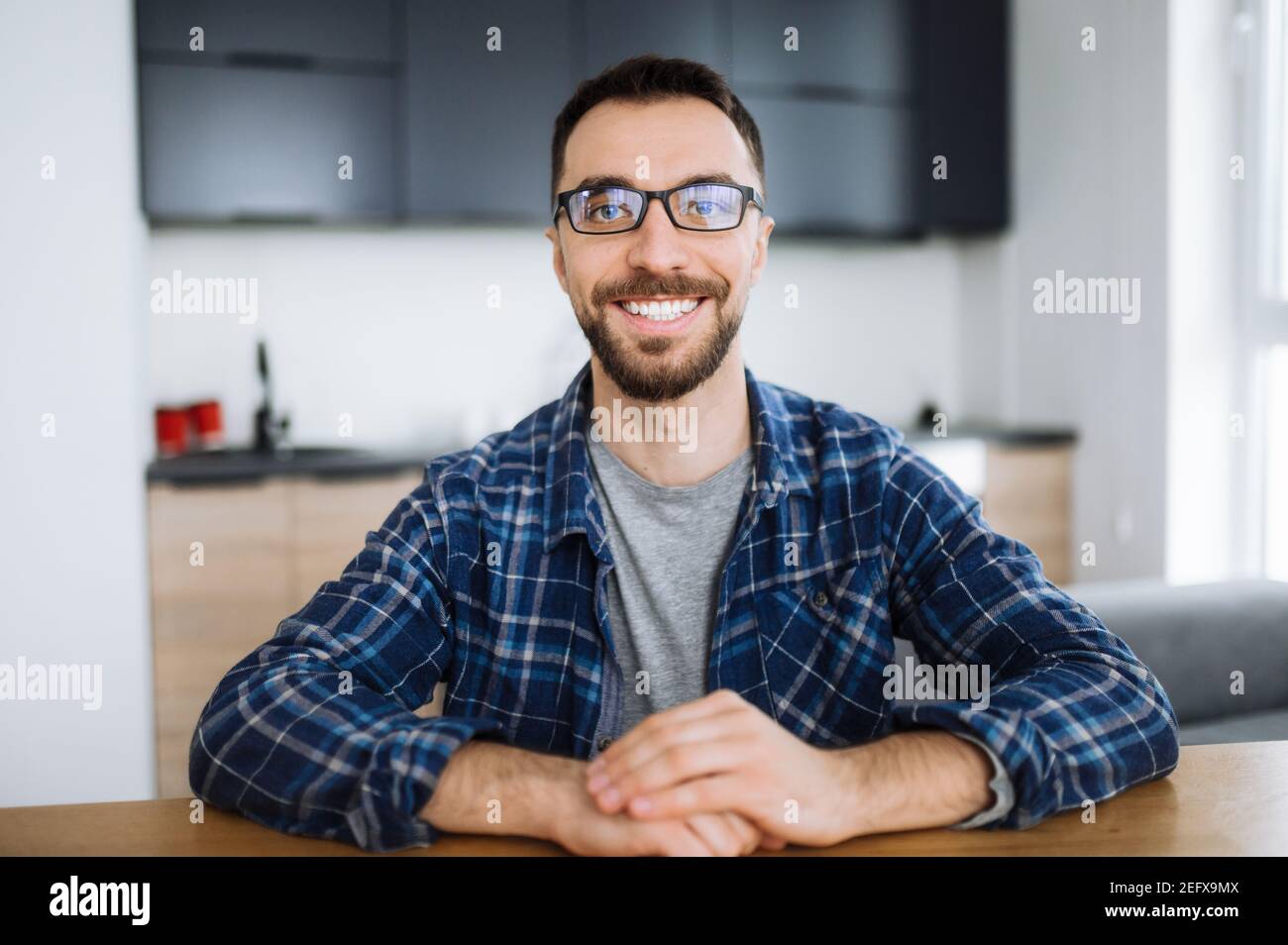 Webcam portrait of happy freelancer guy during video conference, he looks at the camera and smiling. Young adult stylish intelligent man wearing eyeglasses distantly works from home Stock Photo