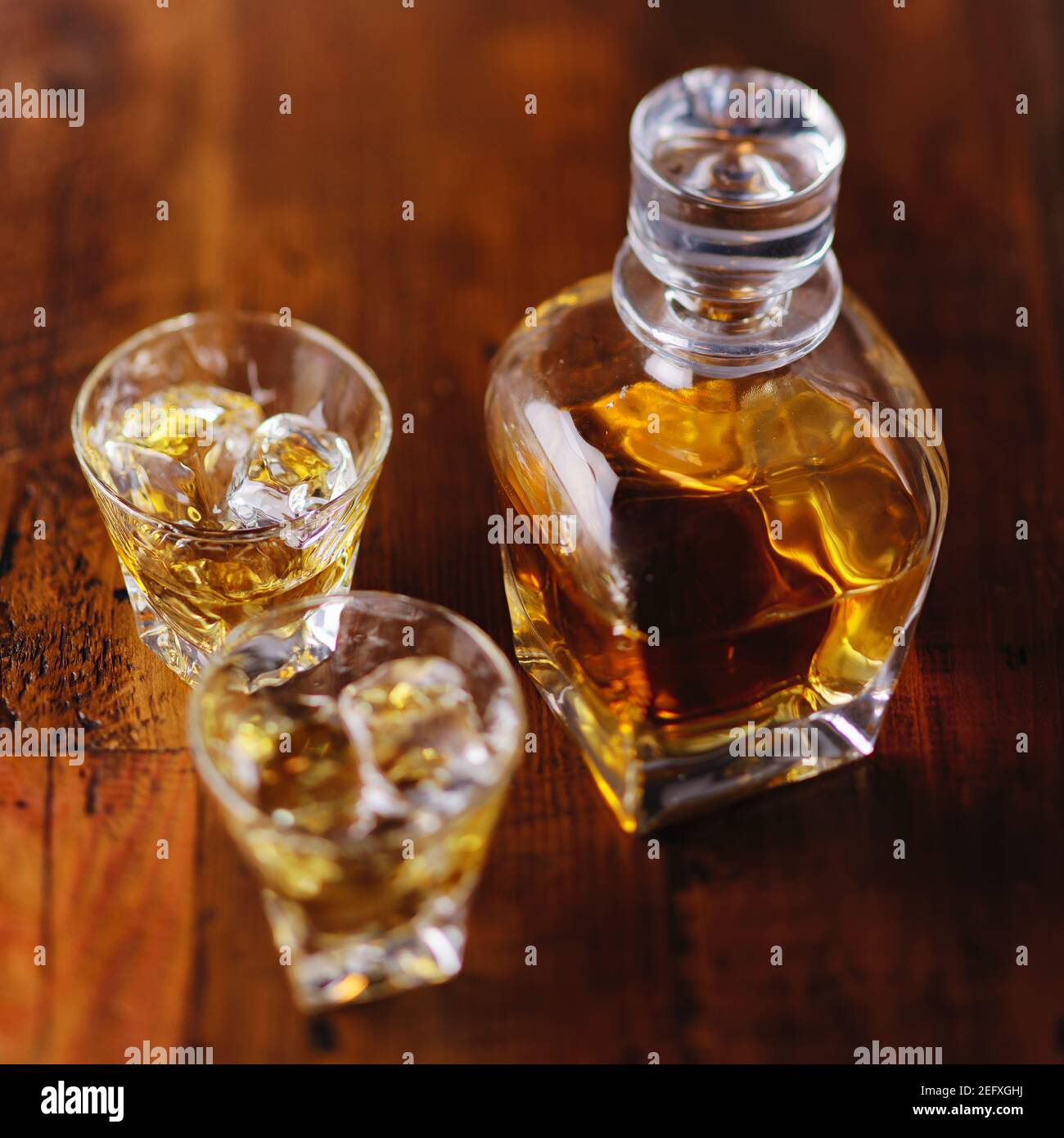 A Whiskey Bottle and Two Glasses of Scotch on the Rocks on a Wooden Table Stock Photo