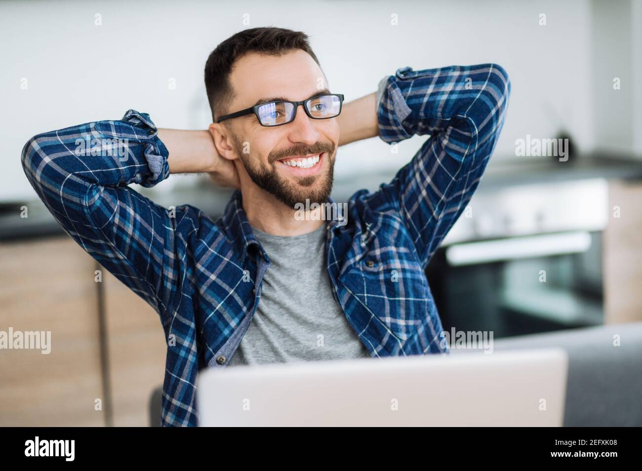 Positive freelancer guy relaxing at the workplace and smiling. Confident caucasian male entrepreneur sitting at home office, taking break from distant working and dreaming about vacation Stock Photo