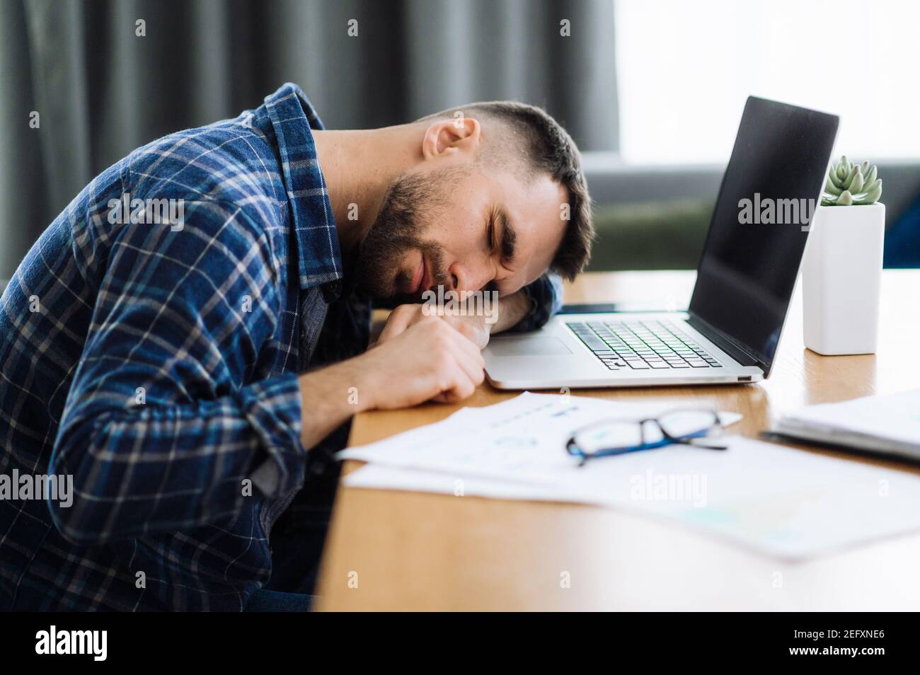 Tired freelancer man is fall asleep at the workplace. Exhausted busy guy working overtime, sits at the desk at home, need a rest, overwork concept. Work from home Stock Photo