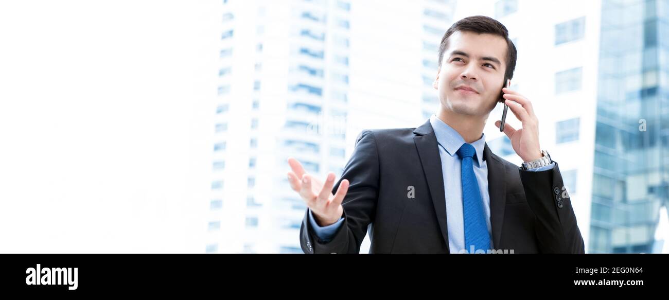 Businessman calling on smartphone with hand gesture in blur office building background - panoramic banner Stock Photo