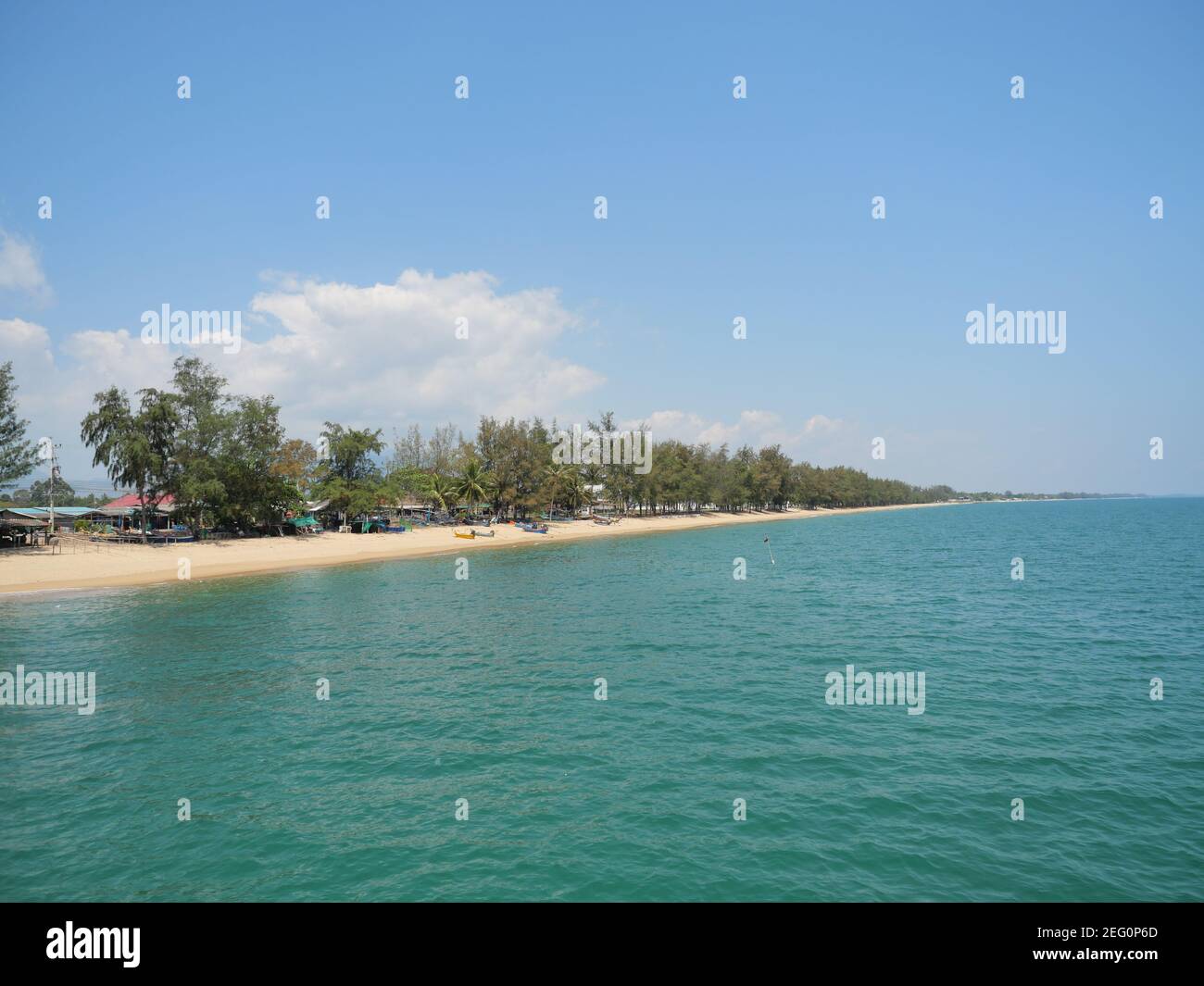 Green water in the sea with a fishing village on the brown sand beach with blue sky and white cloud in background, Prachuap Khiri Khan, Thailand Stock Photo