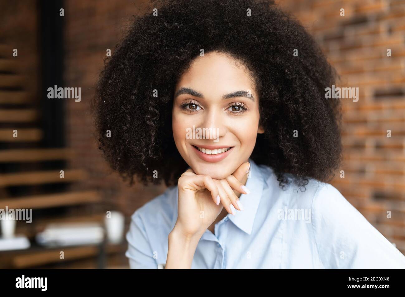 Portrait headshot of young intelligent African American ethnic female with Afro curly hairstyle and beautiful smile, placed hand on chin, looking at Stock Photo