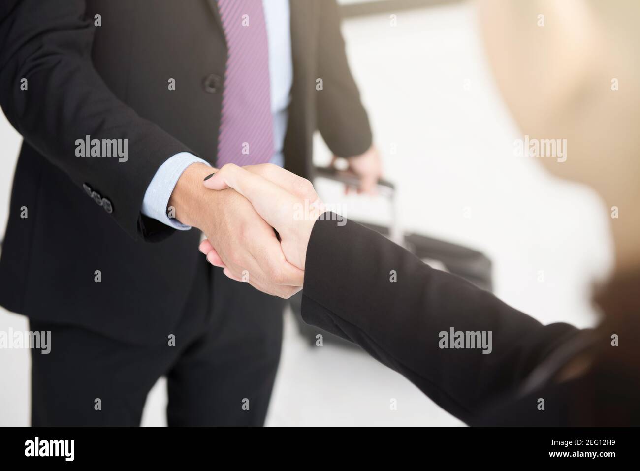 Businessman making handshake while pulling luggage at the airport Stock Photo