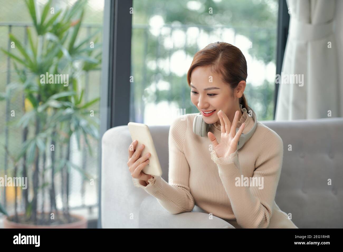 Photo of charming lady holding telephone making selfies speaking skype waving palm saying hi sitting comfort sofa wear casual checkered shirt apartmen Stock Photo