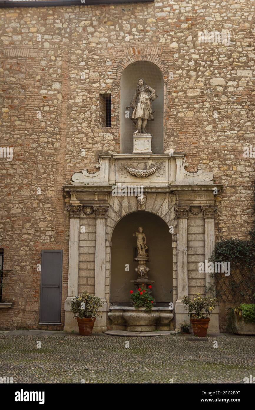 Old sculpture with small fountain and plants and flowers in pots Stock Photo