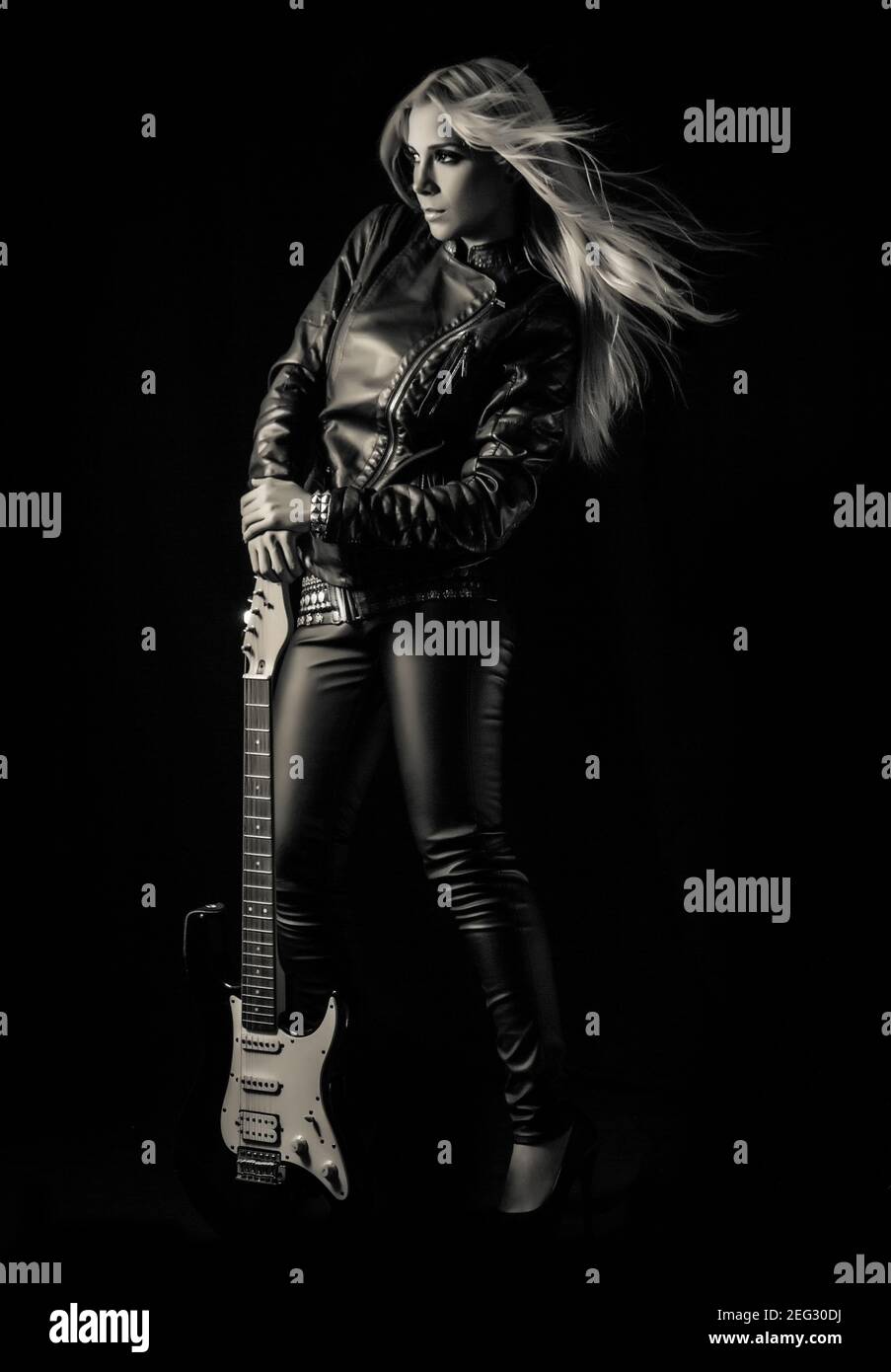 Woman in rocker style clothes posing with a guitar on black background ...