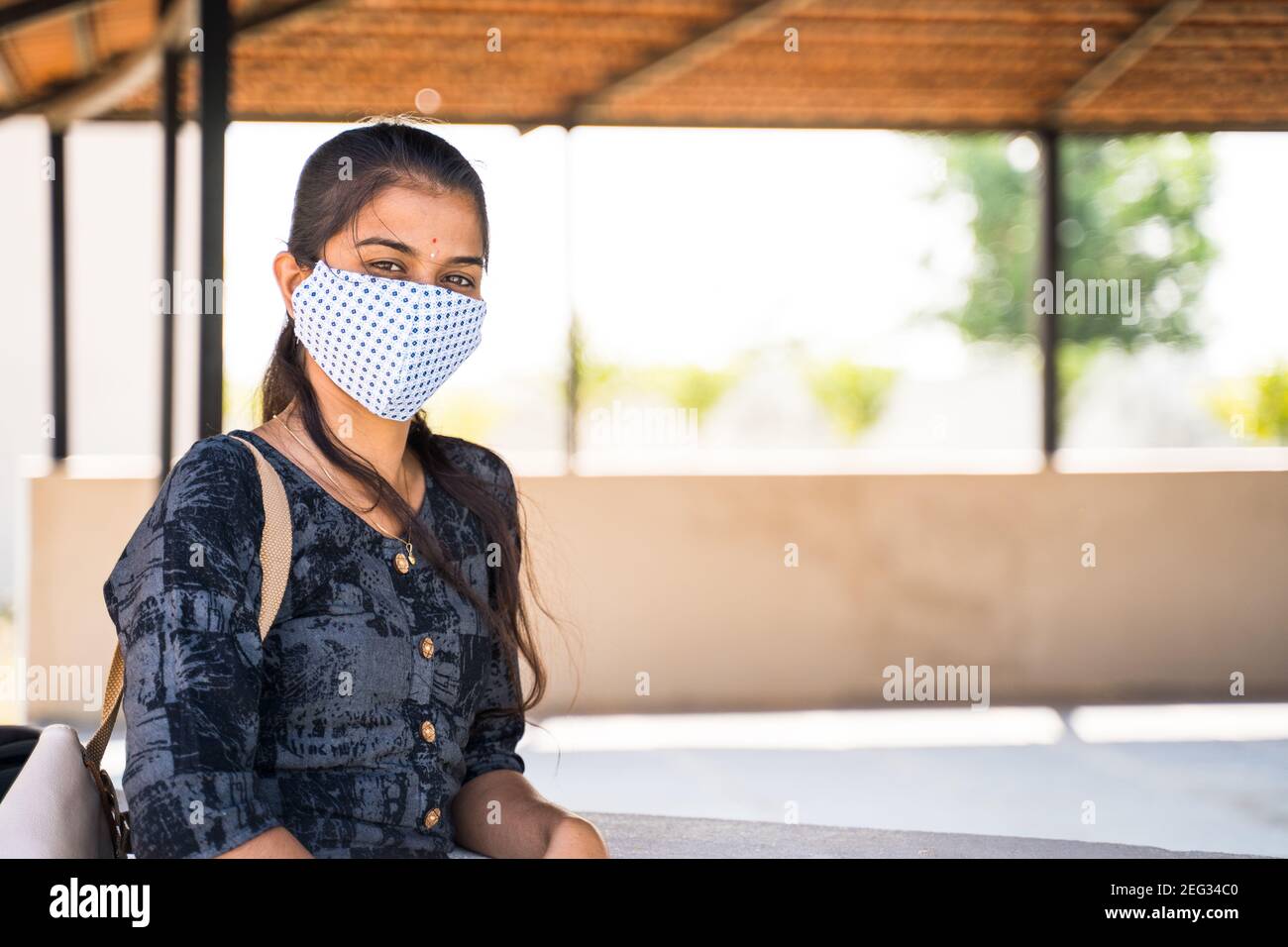 Young Indian girl with medical face mask looking camera at college campus with copy space during coronavirus covid-19 pandemic. Stock Photo