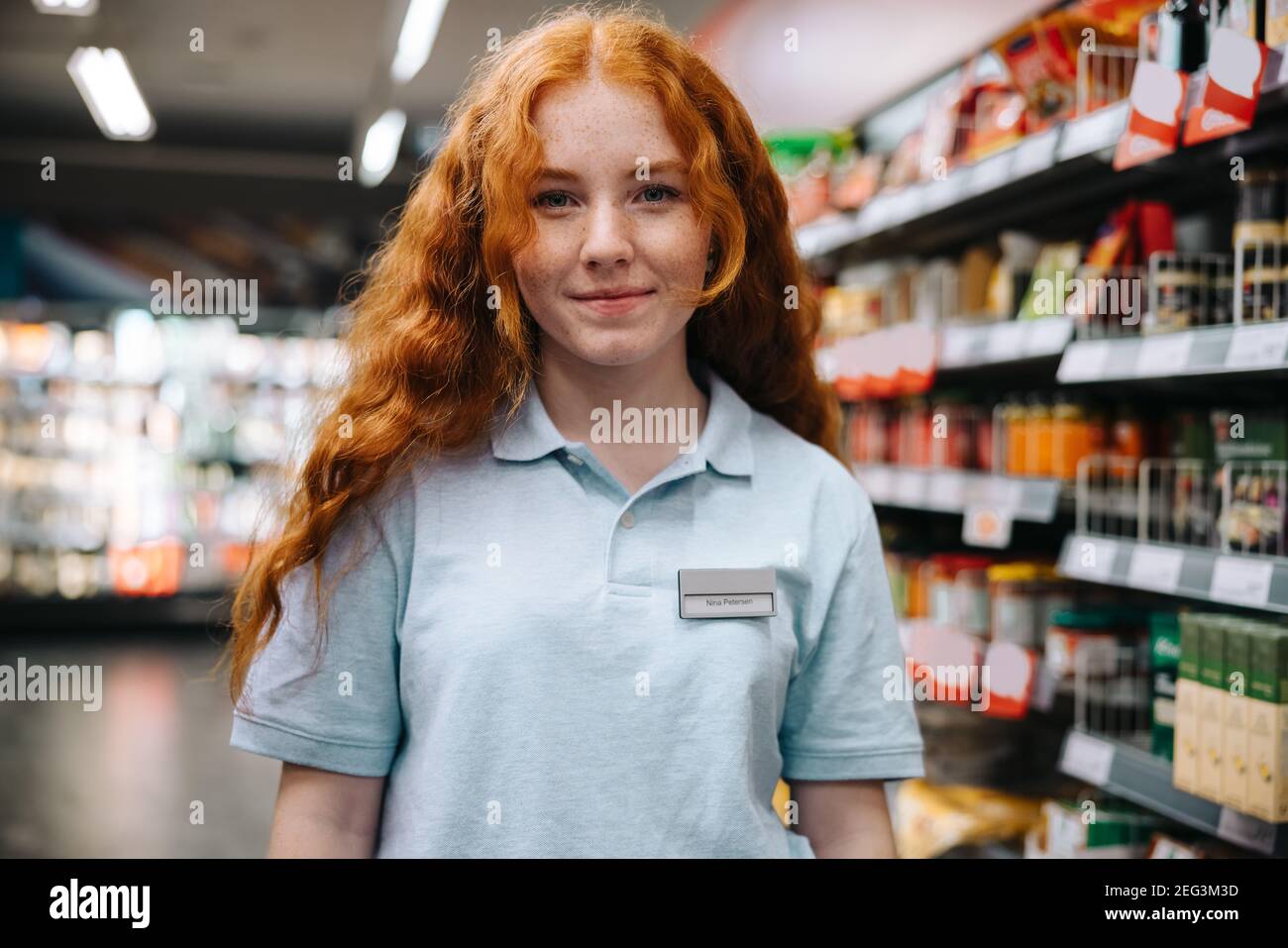 Supermarket trainee employee. Young woman worker on holiday job at grocery shop. Stock Photo