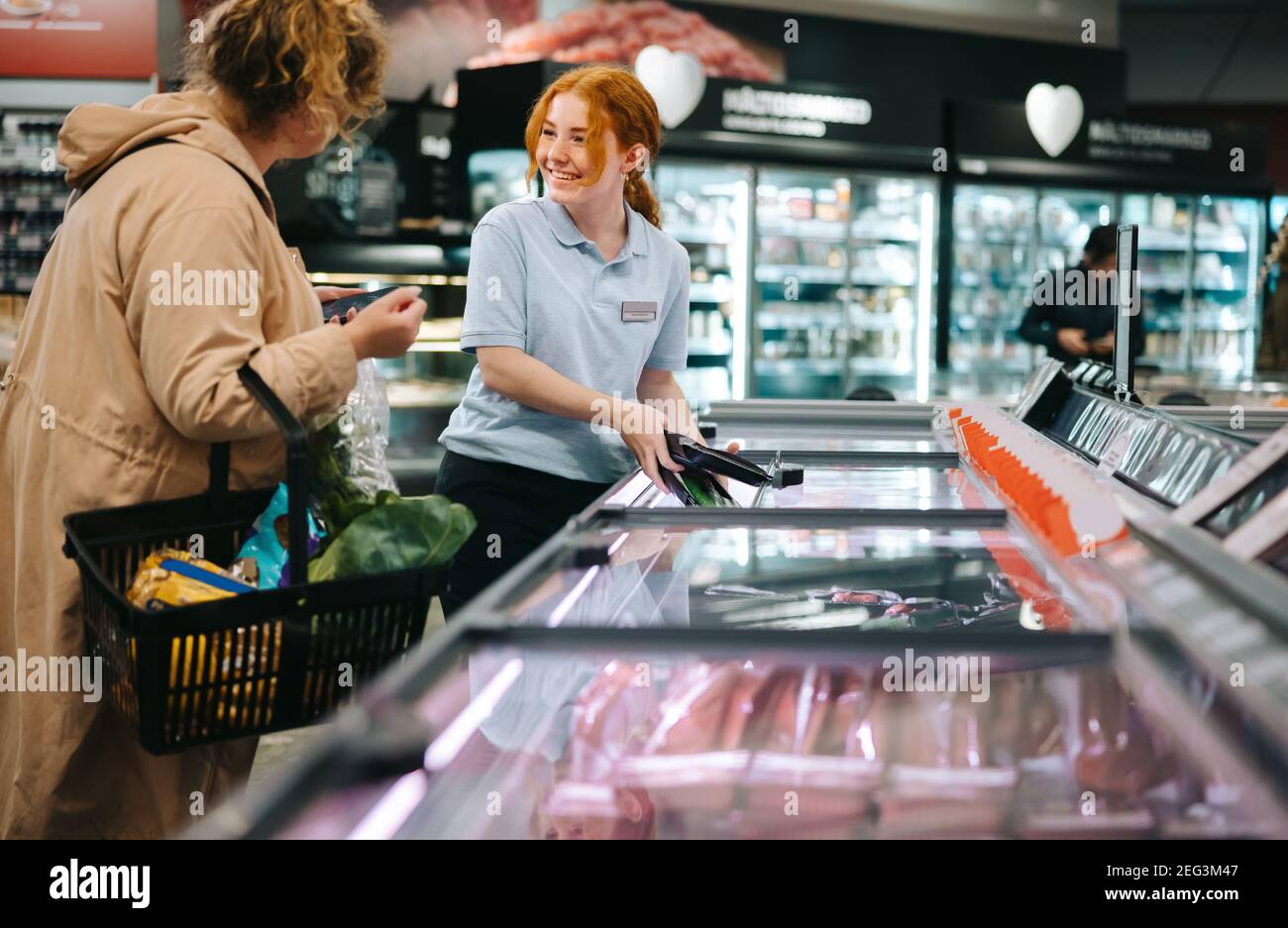 Woman working in supermarket assisting a customer. Grocery shop employee helping a female shopper. Stock Photo