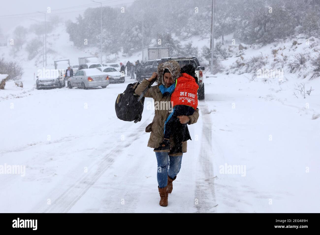 Ajloun, Jordan. 17th Feb, 2021. A woman carrying her child walks in snow in Ajloun, Jordan, on Feb. 17, 2021. A snowstorm on Wednesday hit Jordan's mountainous areas accompanied by heavy winds and cold weather. Credit: Mohammad Abu Ghosh/Xinhua/Alamy Live News Stock Photo