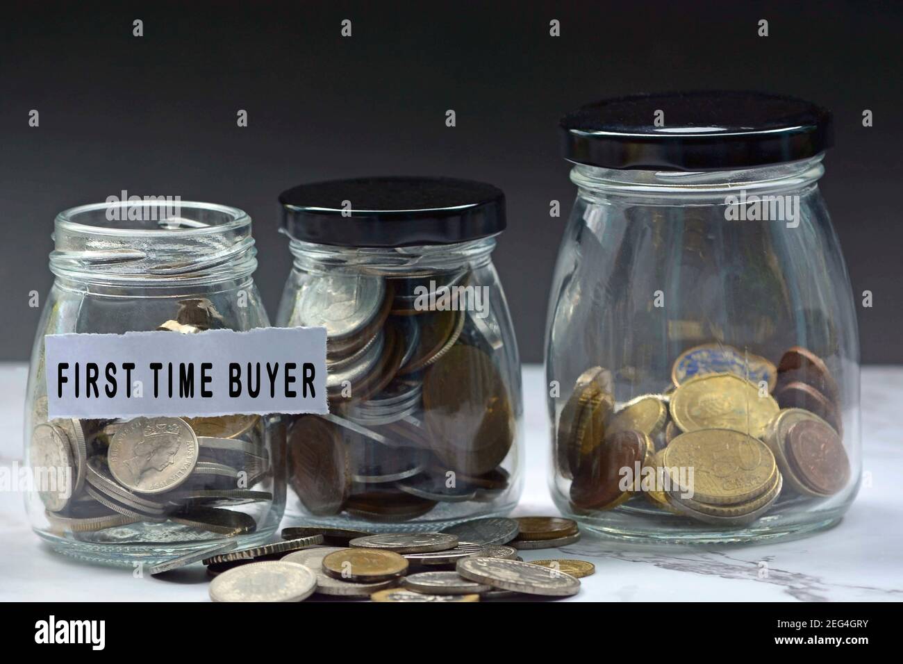 Glass jars with multicurrency coins and text - First time buyer. Home buyer concept Stock Photo