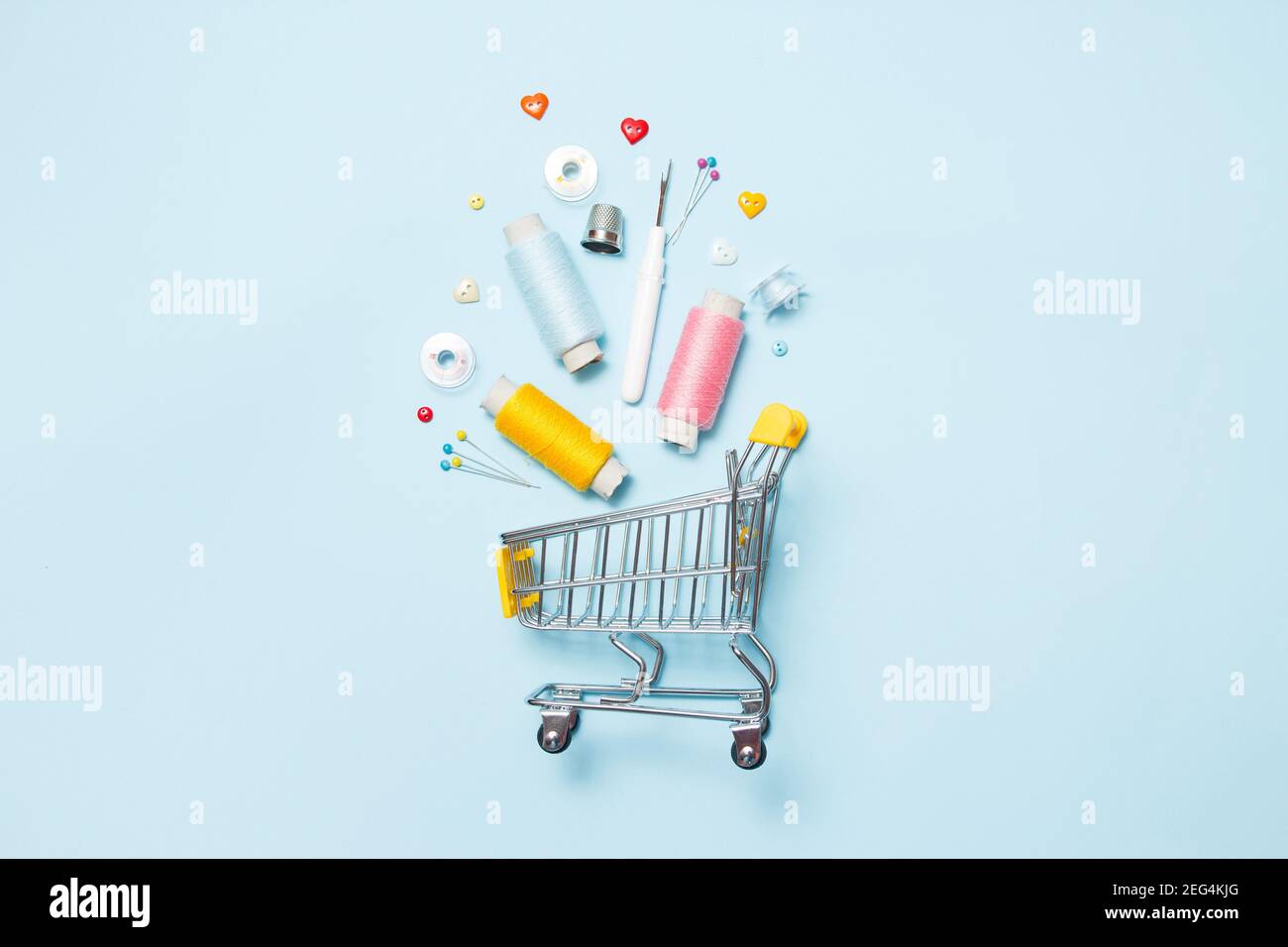 Supermarket cart with sewing accessories on blue background, stitching, embroidery. Space for text, flat lay, top view. Sew background. Sale concept. Stock Photo