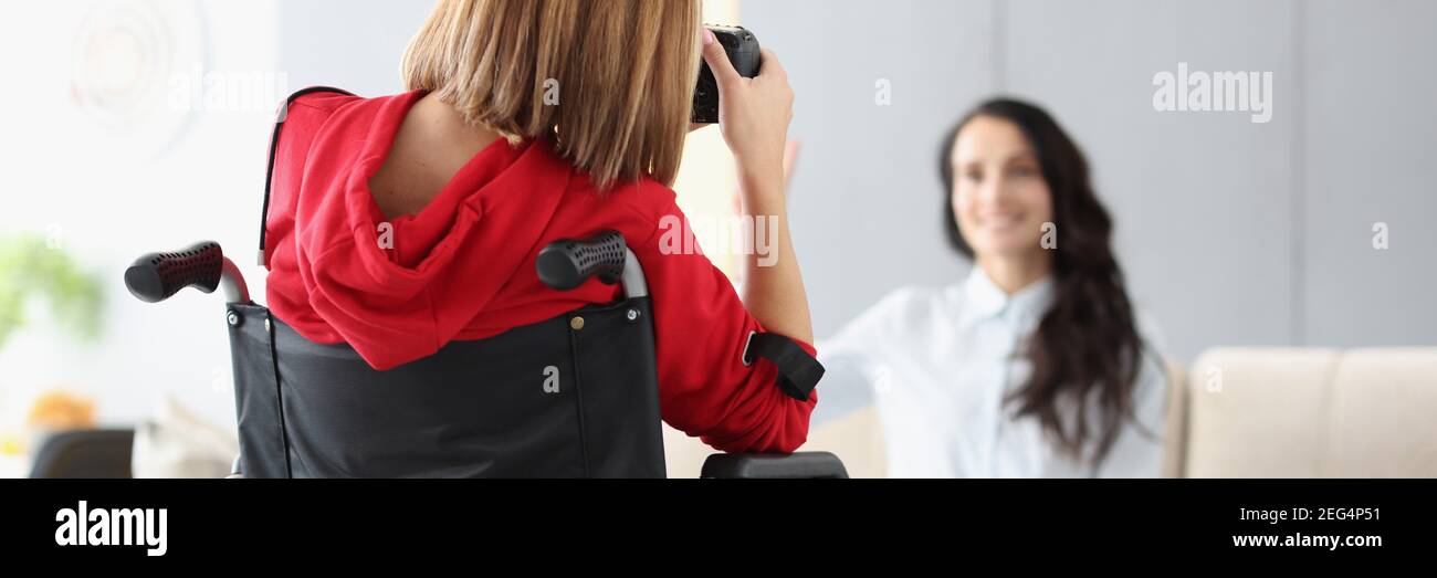 Woman photographer in wheelchair photographs model in background in photo studio close-up Stock Photo