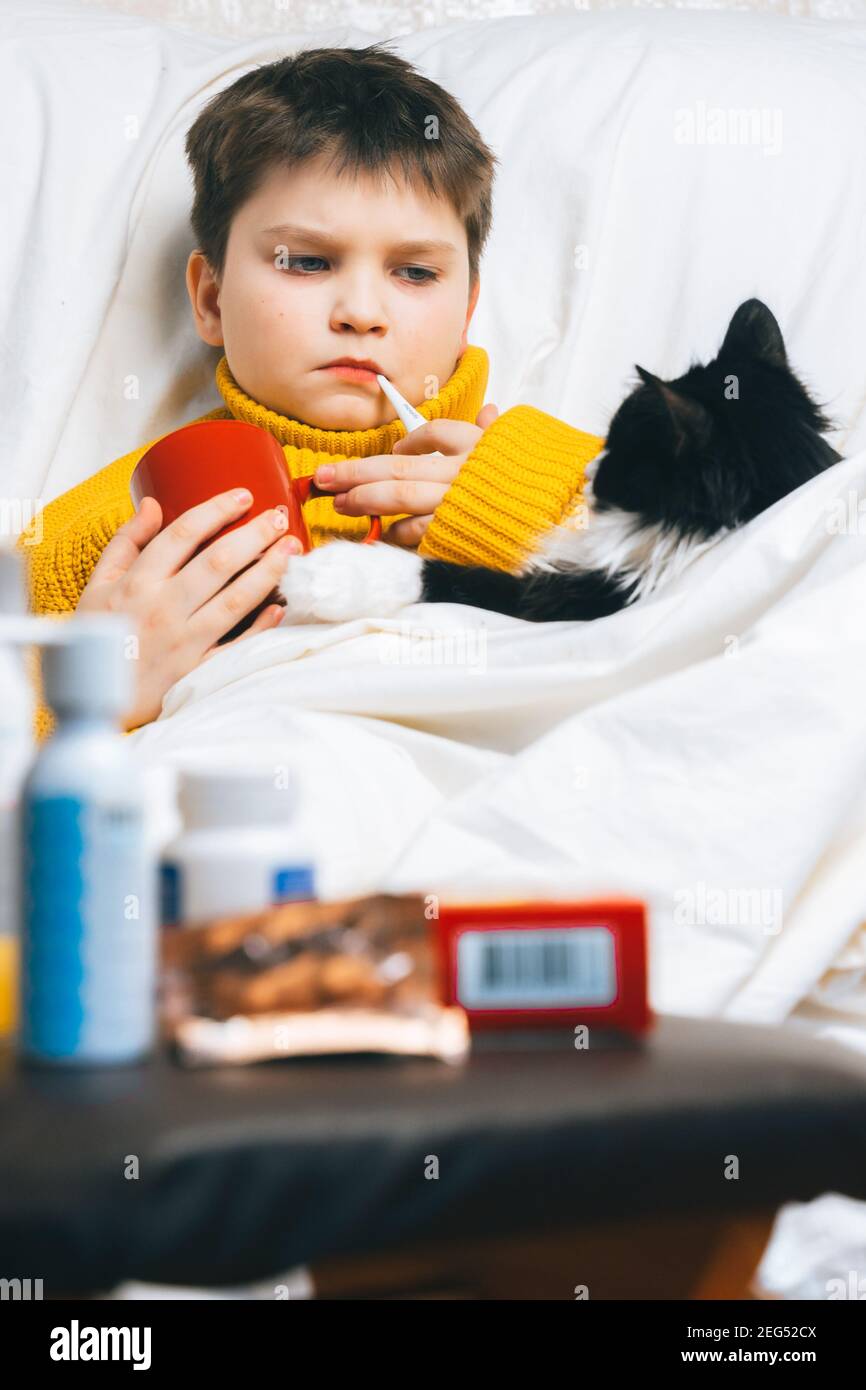 Sick child boy with digital thermometer in mouth lying in bed with