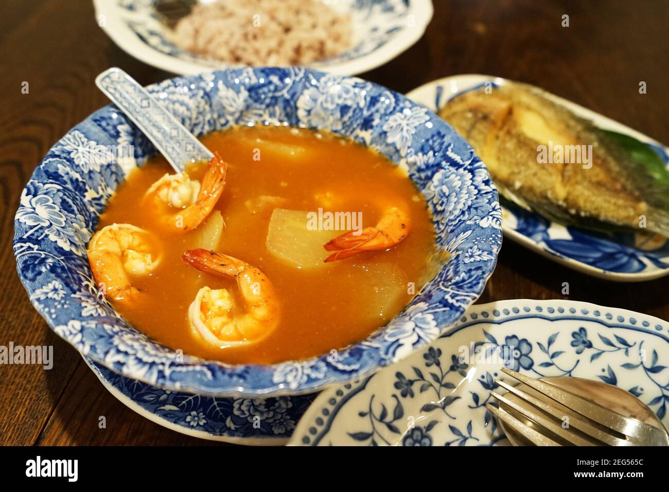 Shrimp sour curry soup served with deep fried Gourami (Gouramy) fish and brown rice Stock Photo