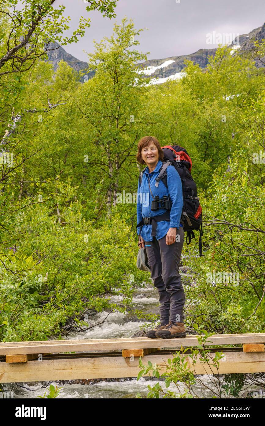 Woman hiking having a backpack on her back crossing a creek on a wooden bridge in Stora sjöfallets nationalpark, Swedish Lapland, Sweden Stock Photo