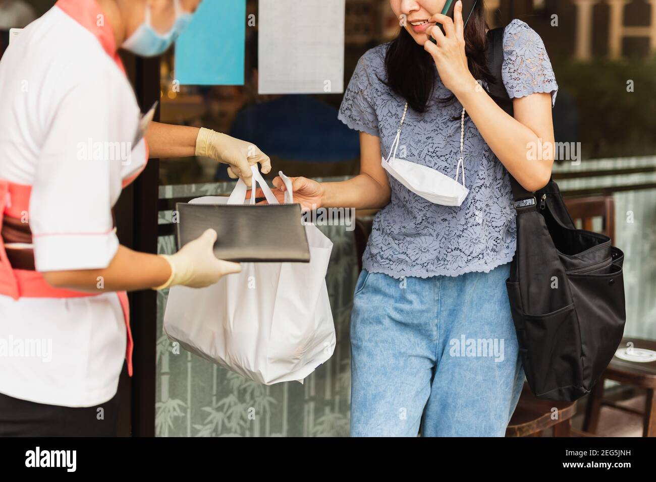 Waitress with protective mask giving take out food bag to woman customer. Stock Photo