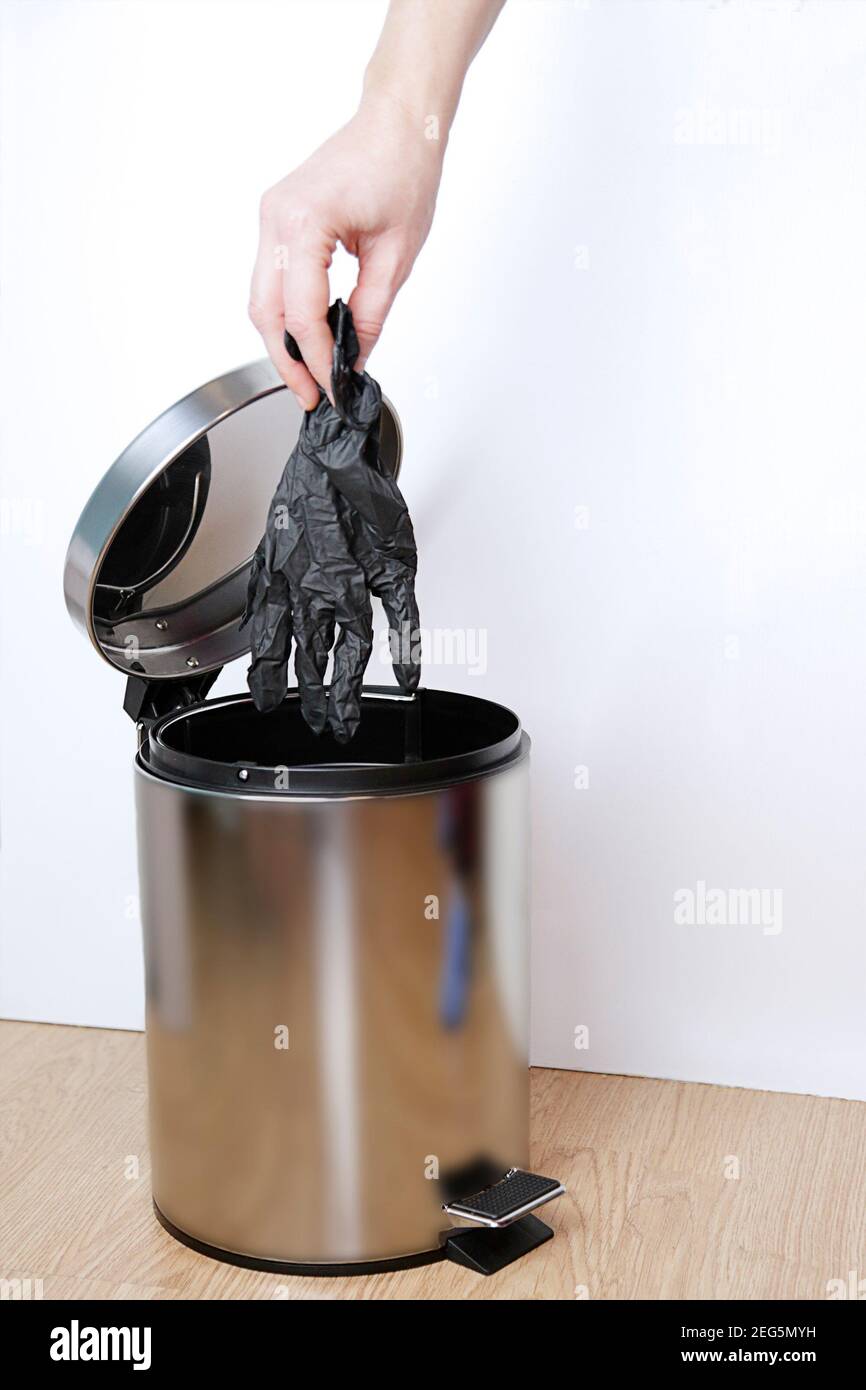 Woman hand throwing black medical gloves into the garbage bin against