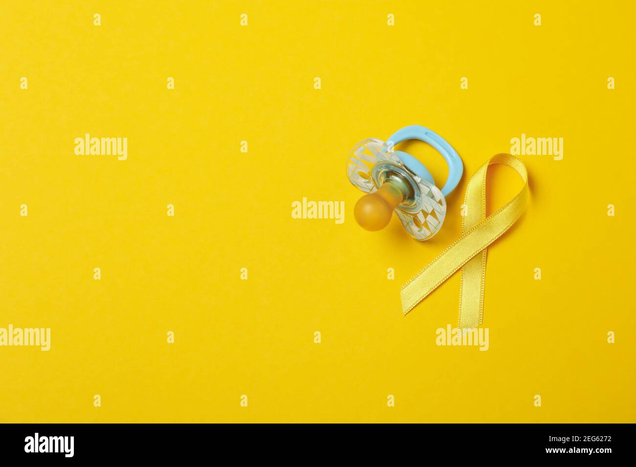 Pacifier and child cancer awareness ribbon on yellow background Stock Photo