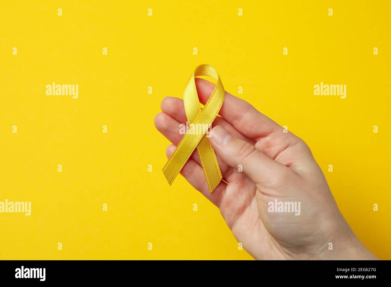 Female hand hold child cancer awareness ribbon on yellow background Stock Photo