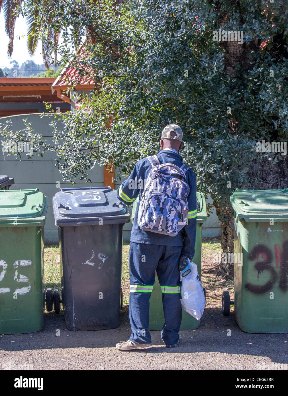Johannesburg, South Africa - unidentified black man digs in residential refuse bins standing on a street in the city Stock Photo