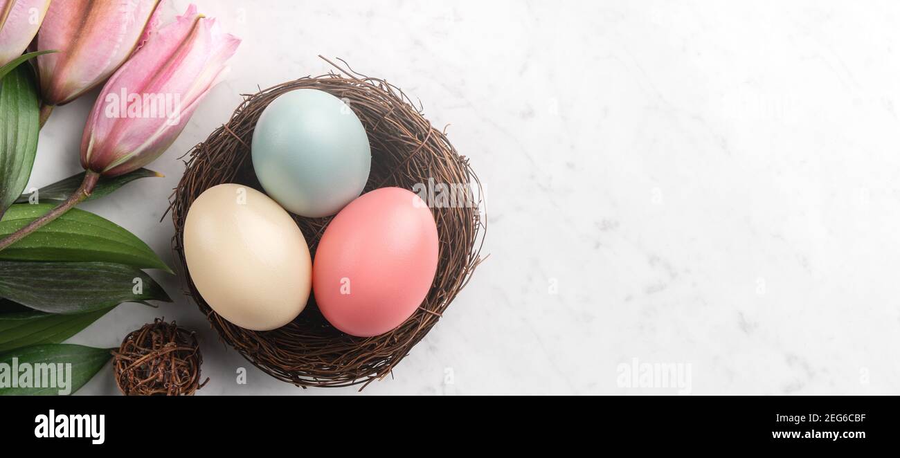Colorful Easter eggs in the nest with pink lily flower on bright marble ...
